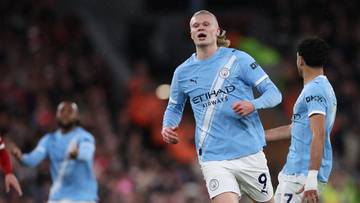 Piłkarz Manchesteru City Erling Haaland z podniesioną ręką, w tle inny piłkarz w jasnobłękitnej koszulce.