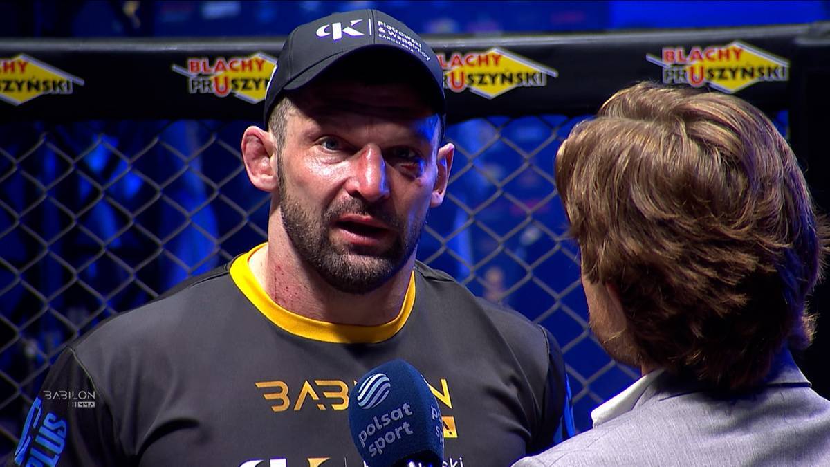 Mężczyzna w czapce z daszkiem i koszulce sportowej udziela wywiadu z mikrofonem.