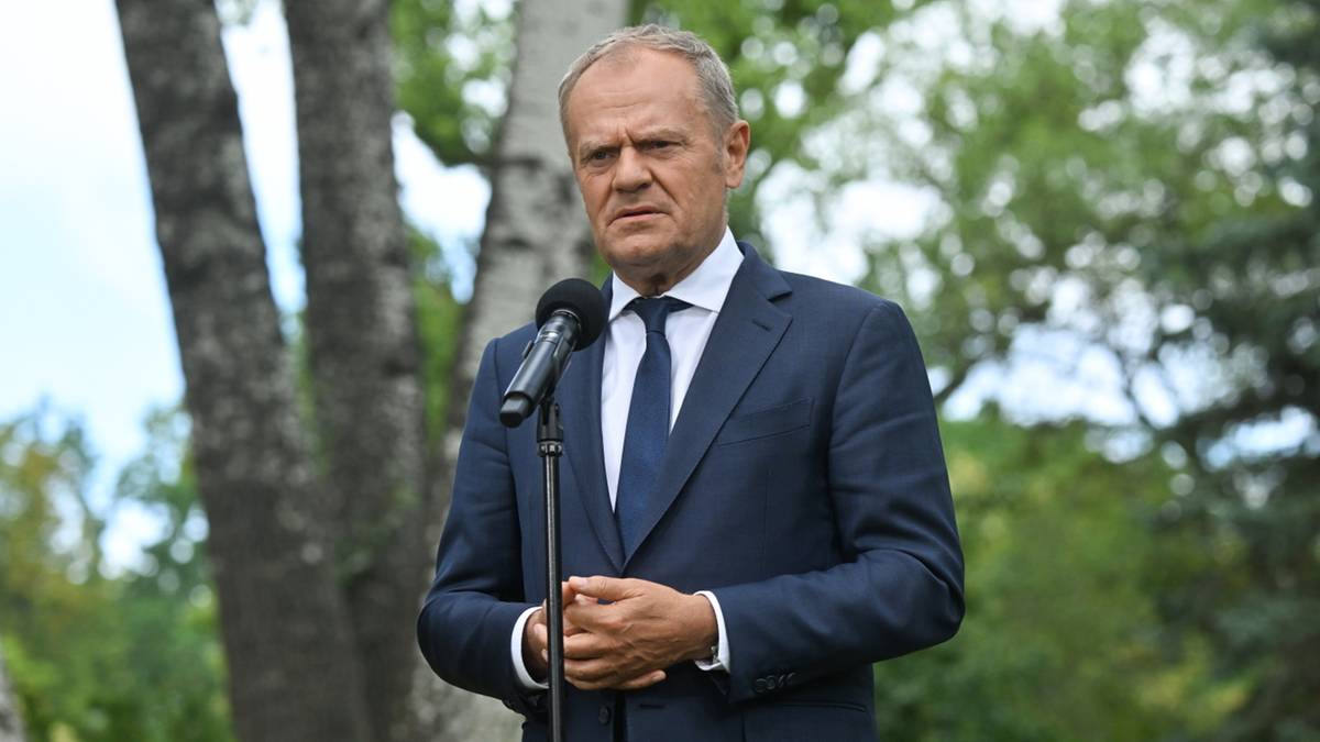 Donald Tusk przemawia do mikrofonu stojąc w plenerze na tle drzew.