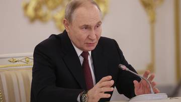 Władimir Putin siedzi przy stole w garniturze i rozmawia.