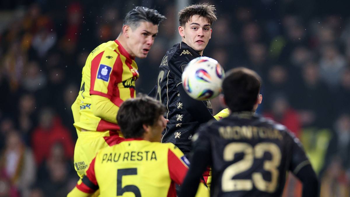 Czterech piłkarzy w akcji podczas meczu piłki nożnej, dw&oacute;ch w ż&oacute;łto-czerwonych strojach i dw&oacute;ch w czarnych.