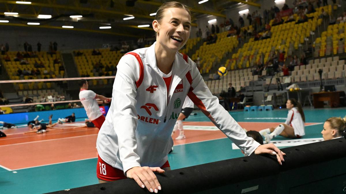 Uśmiechnięta siatkarka w stroju reprezentacji Polski, opierając się o bandę na boisku.