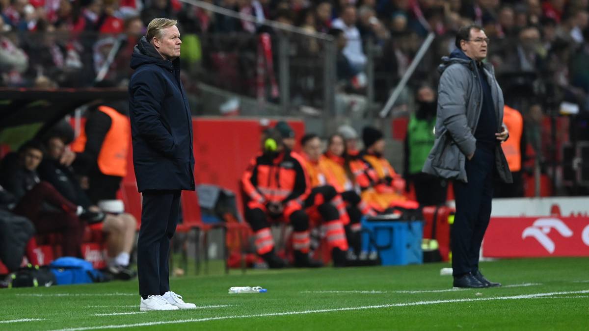 Dw&oacute;ch trener&oacute;w piłkarskich stoi na boisku, jeden w ciemnym płaszczu, drugi w jasnej kurtce.