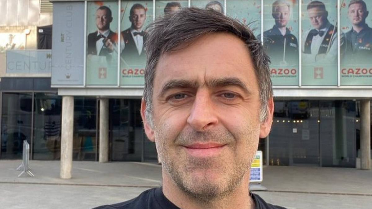 Zbliżenie na twarz Ronniego O'Sullivana, z billboardami przedstawiającymi innych graczy snookera w tle.