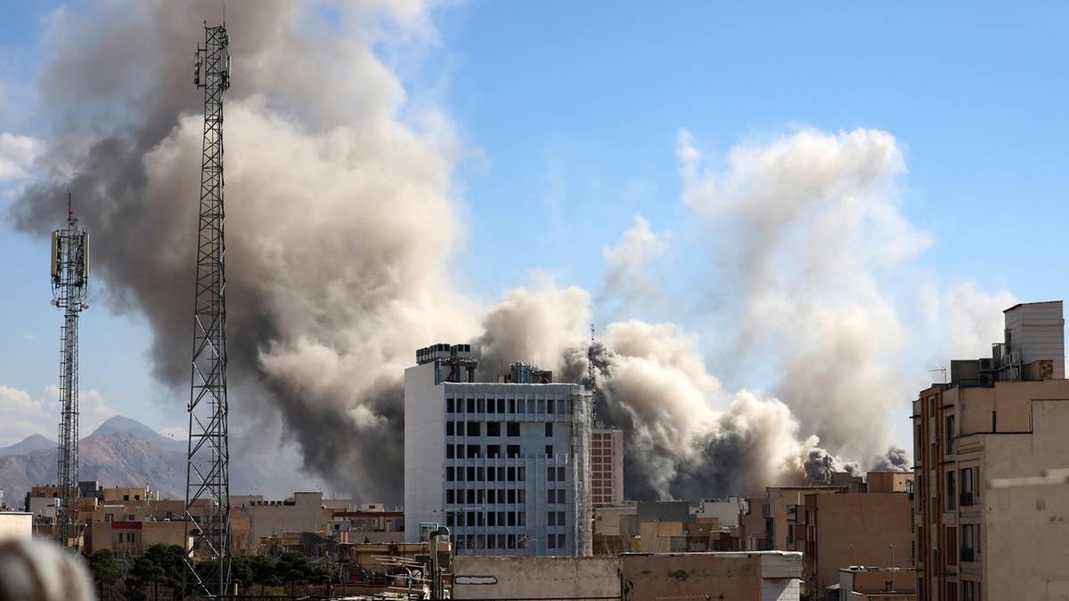 Widok miasta z budynkami i wieżami telekomunikacyjnymi, nad którymi unosi się gęsty, ciemny dym.