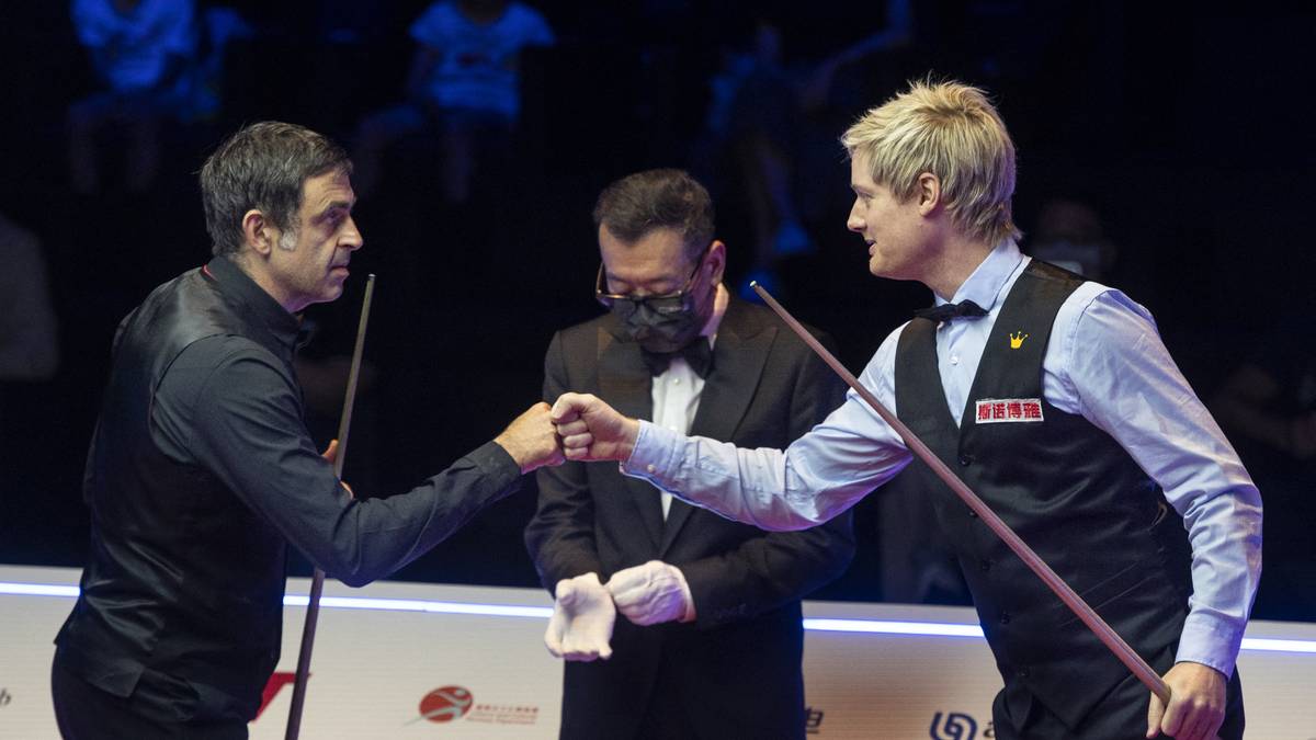 Dwóch graczy snookera wita się uściskiem dłoni przed stołem bilardowym, z sędzią pośrodku.