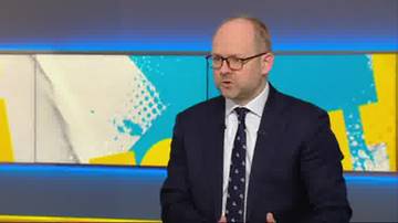 Mężczyzna w okularach i granatowym garniturze z krawatem, m&oacute;wiący podczas wywiadu lub programu telewizyjnego.