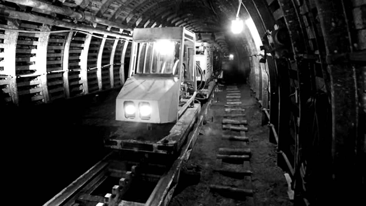 Wnętrze tunelu kopalnianego z szynami i pojazdem g&oacute;rniczym