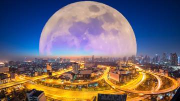 Widok nocnego miasta z ogromnym Księżycem na niebie.