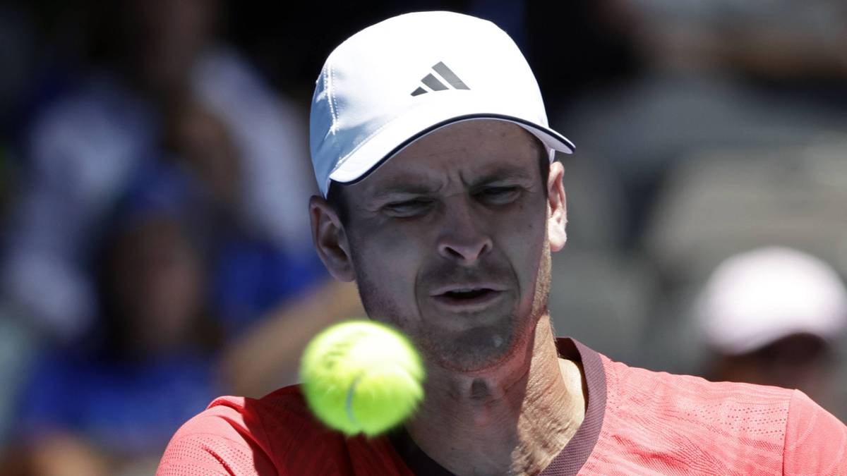 Portret męski, tenisista w białej czapce z daszkiem, z bliska, w oddali rozmyte sylwetki innych os&oacute;b. Na pierwszym planie leci ż&oacute;łto-zielona piłeczka tenisowa, skupiająca uwagę gracza.