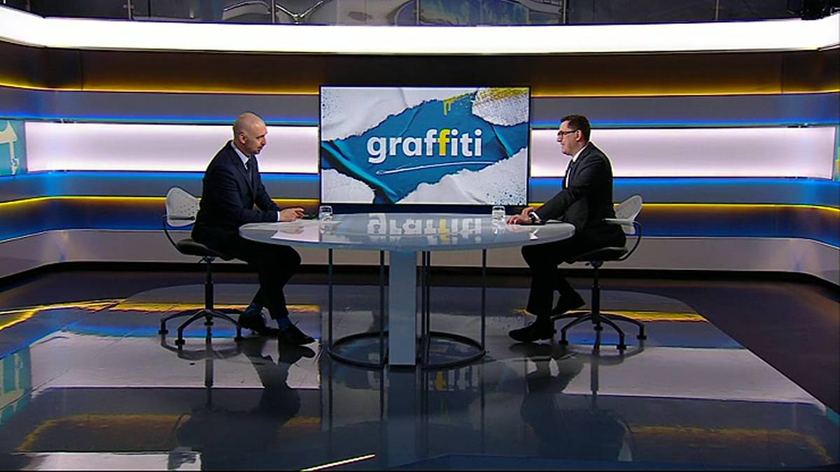 Dw&oacute;ch mężczyzn siedzi przy stole w studiu telewizyjnym, naprzeciwko nich widnieje ekran z logo programu "graffiti".