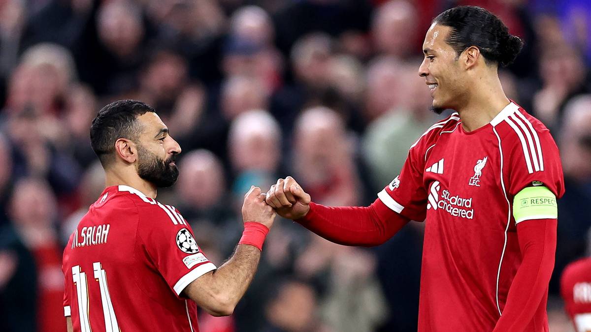 Mohamed Salah i Virgil van Dijk, piłkarze Liverpoolu FC, podają sobie ręce na boisku w czerwonych strojach klubowych.
