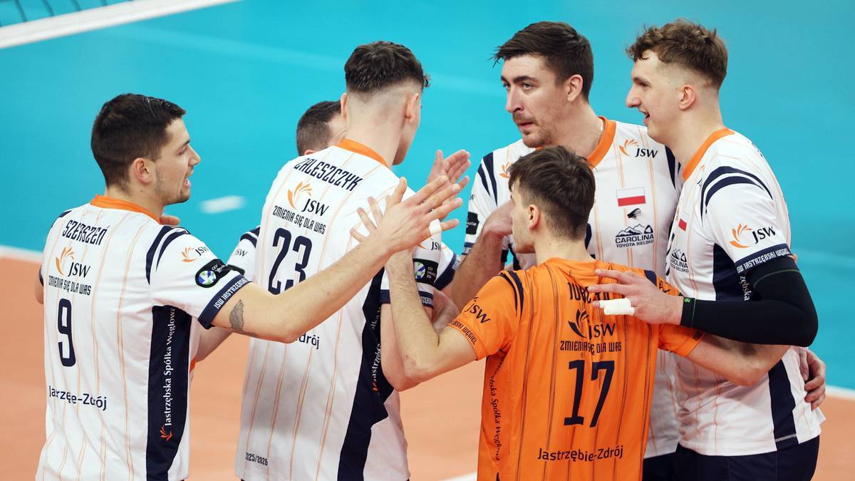 Drużyna siatkarzy świętująca na boisku, ubrana w białe i pomarańczowe stroje.