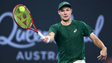 Tenisista Kamil Majchrzak podczas meczu, trzymający rakietę i uderzający piłkę.