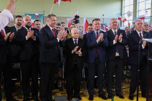 Jarosław Kaczyński i inni politycy stoją na scenie podczas konwencji, klaszcząc.