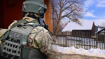 Policjant w kamizelce taktycznej z napisem POLICJA, z widokiem na zaśnieżony płot i dom