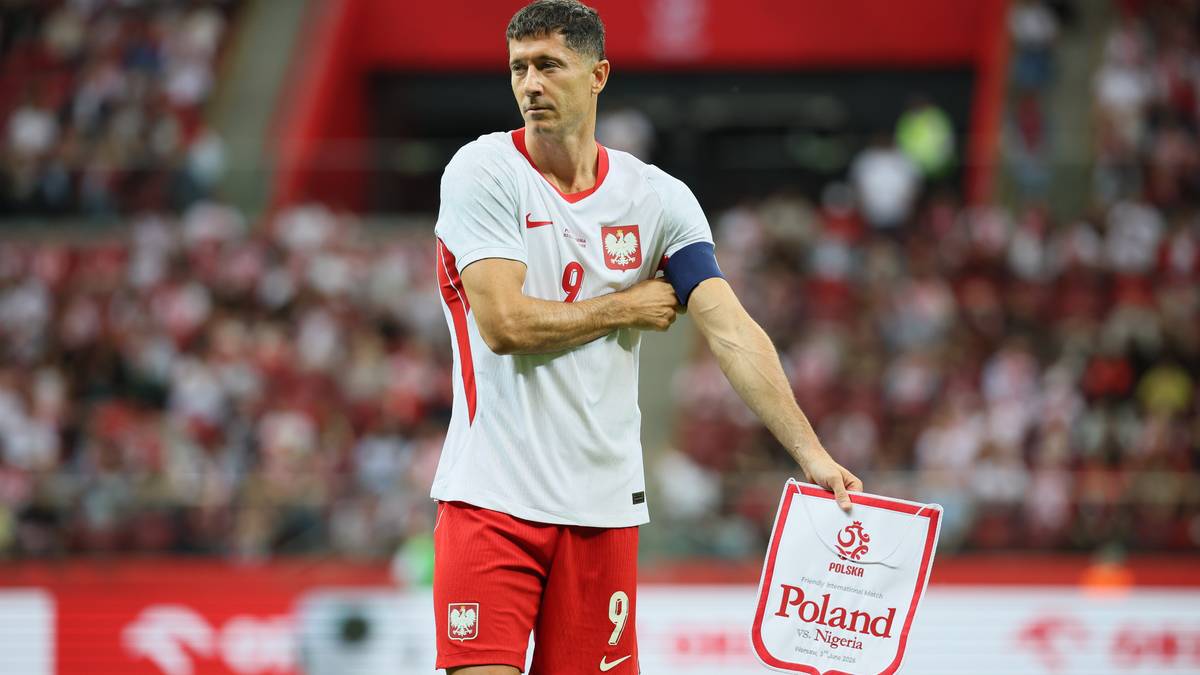 Robert Lewandowski w białej koszulce z czerwonymi elementami i numerem 9, trzymający tabliczkę z napisem Poland.