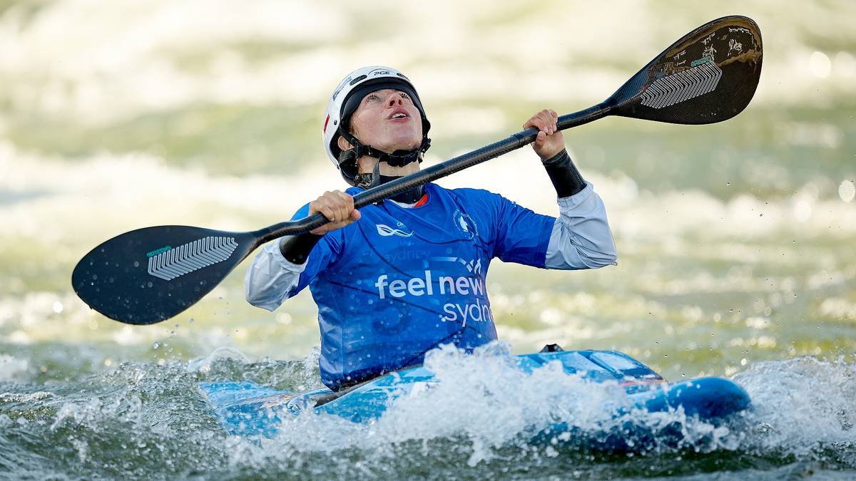Młody zawodnik w kasku siedzi w kajaku, wiosłując i patrząc w górę.
