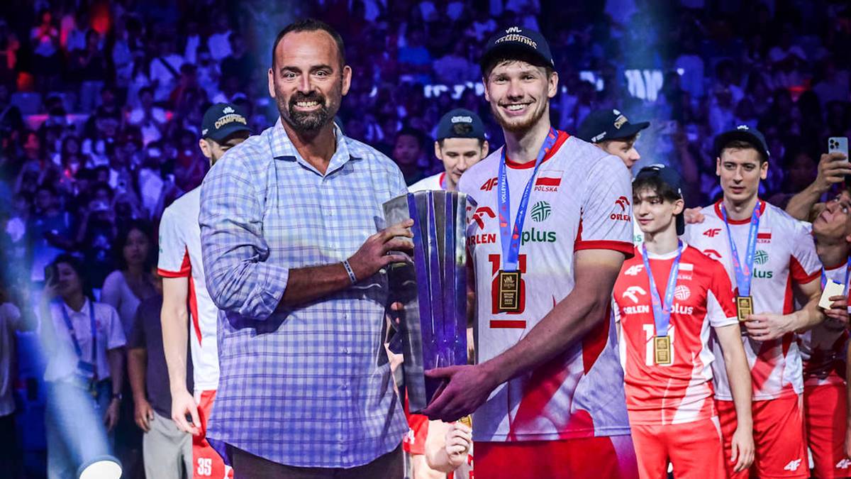 Dw&oacute;ch mężczyzn w strojach sportowych z medalami na szyjach pozuje do zdjęcia z trofeum.