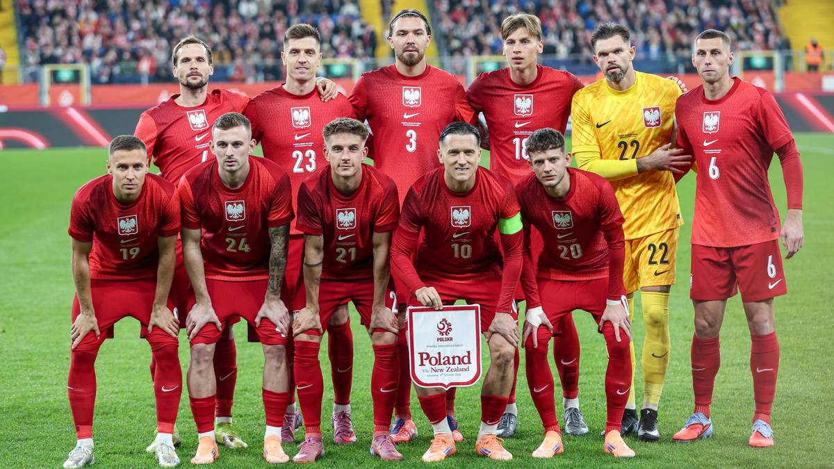 Reprezentacja Polski w piłce nożnej pozuje do zdjęcia na boisku, wszyscy ubrani w czerwone stroje.