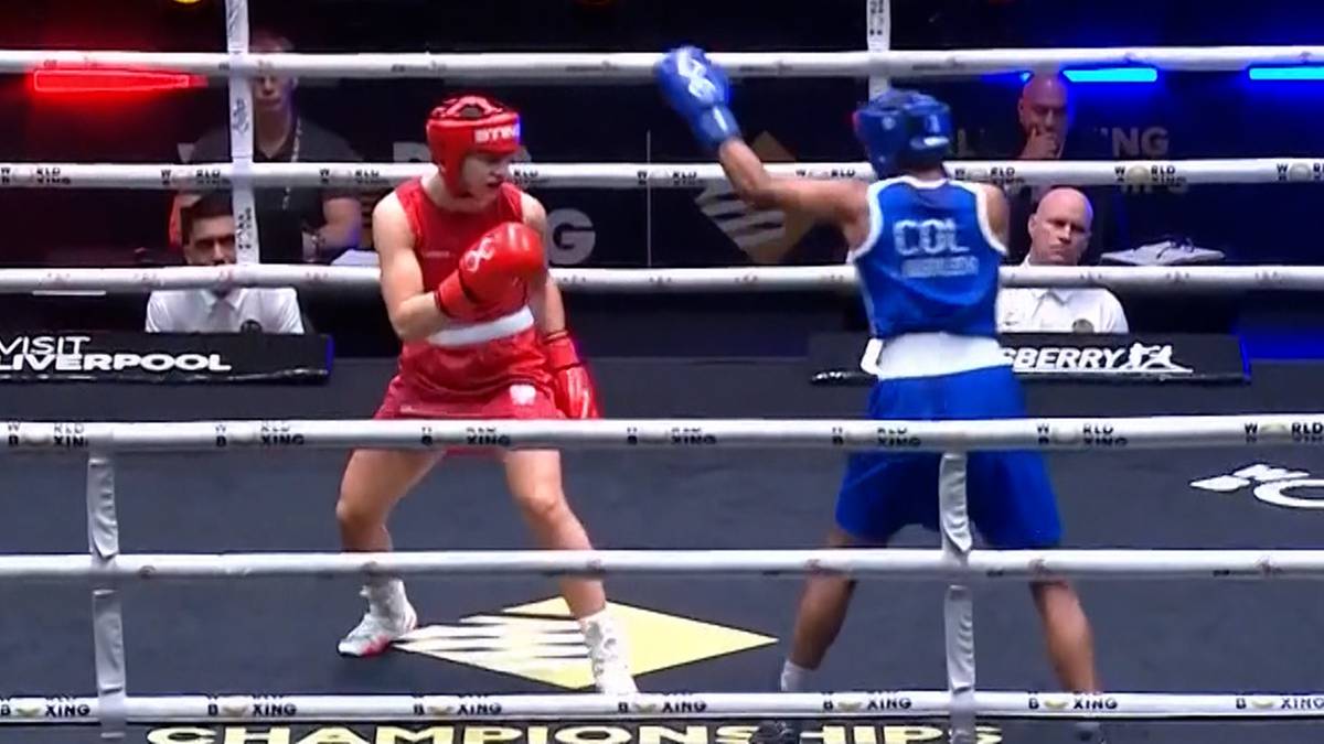 Dwie zawodniczki boksujące w ringu, jedna w czerwonym stroju i z czerwoną rękawicą, druga w niebieskim stroju z rękawicą w górze.