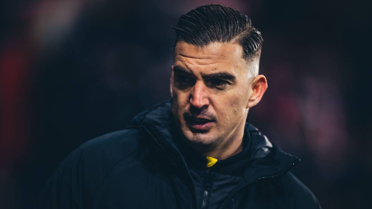 Mężczyzna w czarnej kurtce sportowej z ż&oacute;łtymi akcentami, patrzący w bok.