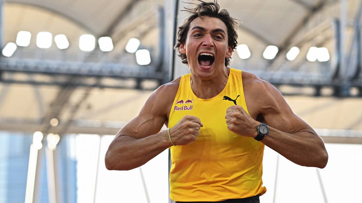 Mężczyzna w żółtej koszulce z uniesionymi pięściami i szeroko otwartymi ustami, wyrażający radość i wysiłek.