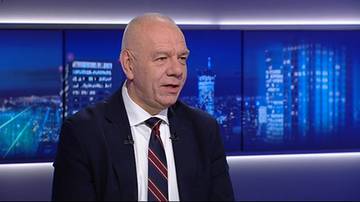 Jacek Sasin, polityk, w garniturze i krawacie, siedzi przed ekranem z widokiem na nocne miasto.