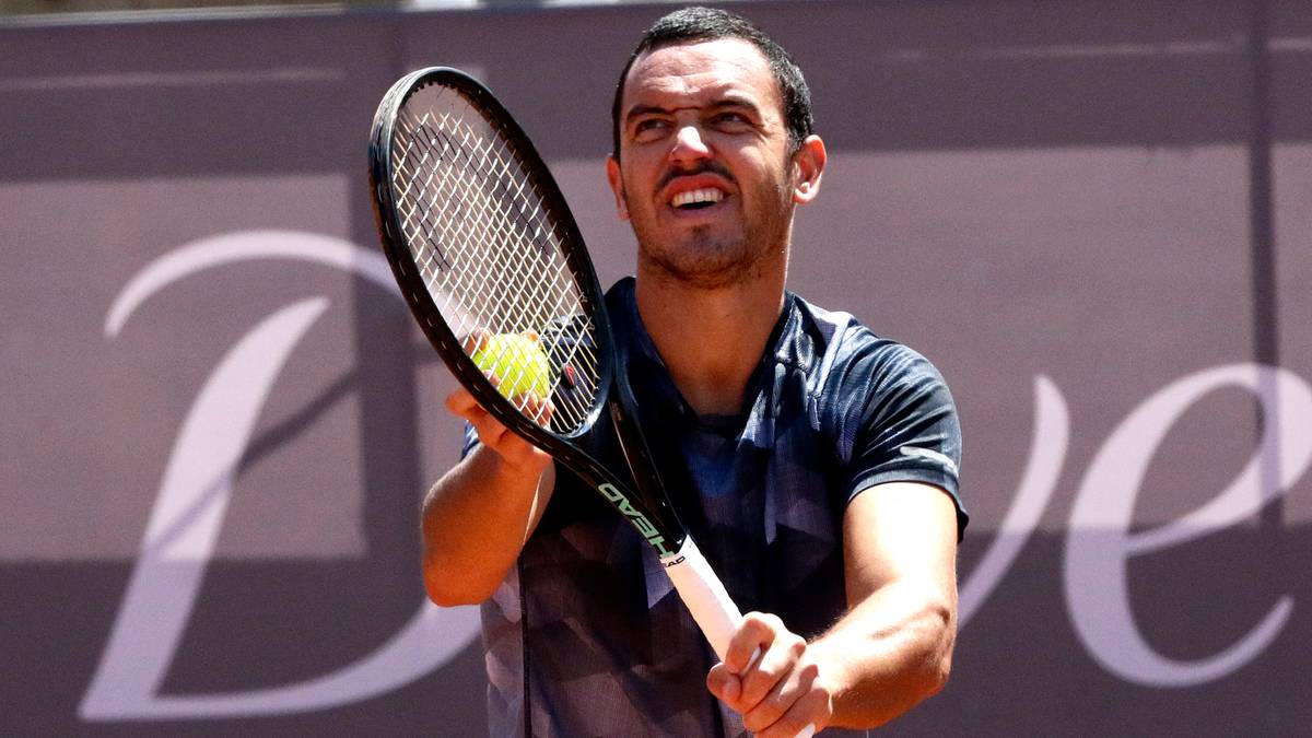 Tenisista z rakietą tenisową i piłką w ręku podczas serwisu.