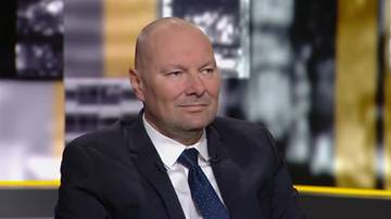 Mężczyzna w garniturze i krawacie siedzi w studiu telewizyjnym.