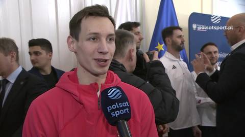 Kacper Tomasiak w czerwonej bluzie z kapturem udziela wywiadu, trzymając mikrofon Polsat Sport. W tle widoczni są inni mężczyźni i flagi.