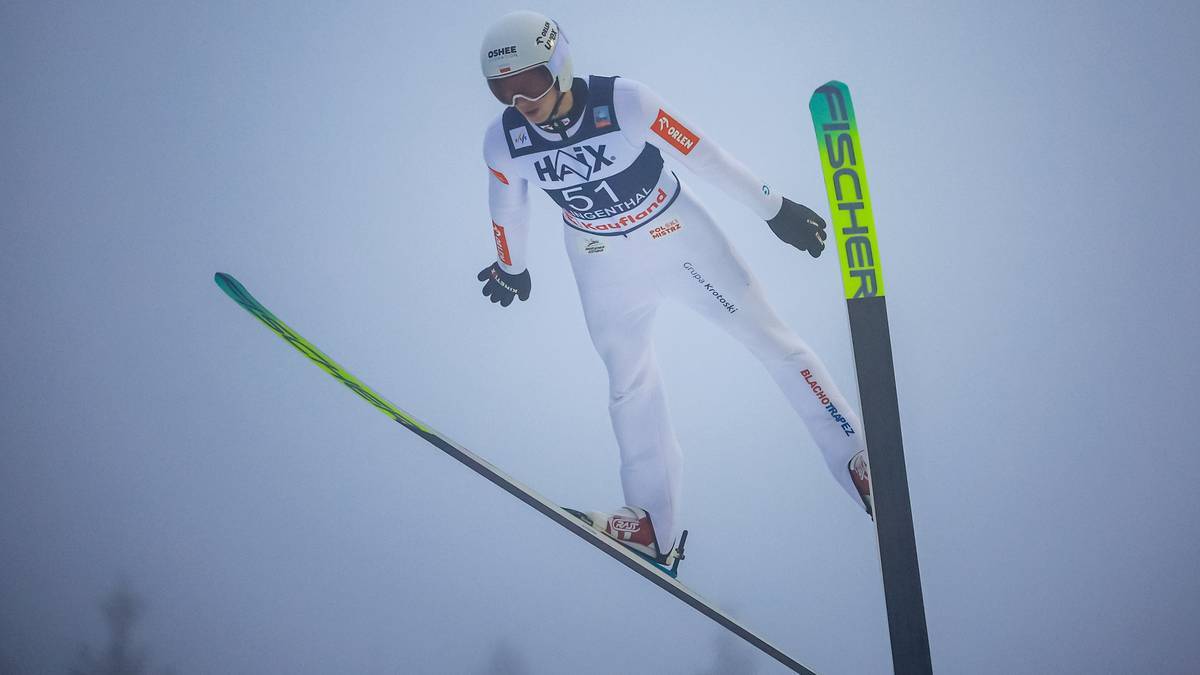 Skoczek narciarski w locie, w białym stroju z numerem 51.