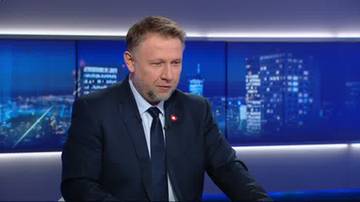 Mężczyzna w garniturze i krawacie, stojący przed ekranami z nocnym widokiem miasta.