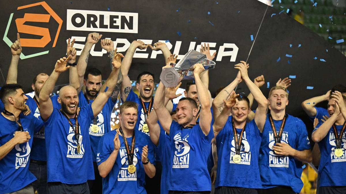 Grupa uśmiechniętych mężczyzn w niebieskich koszulkach, część z nich trzyma podniesione ręce lub podniesione trofeum.