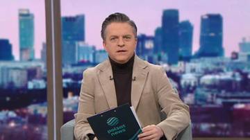 Mężczyzna w beżowej marynarce, siedzi i trzyma teczkę z logo Polsat News. W tle widok na miasto.