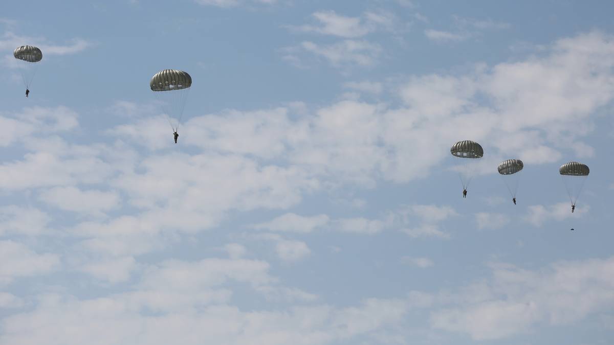 Żołnierze spadają na spadochronach z samolot&oacute;w na tle błękitnego nieba z chmurami.