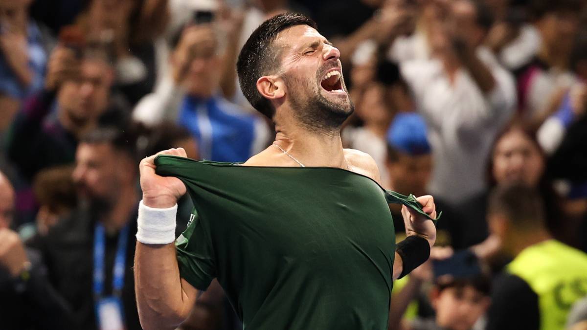 Novak Djoković krzyczy z radości, szarpiąc za koszulkę po wygranej na korcie tenisowym.