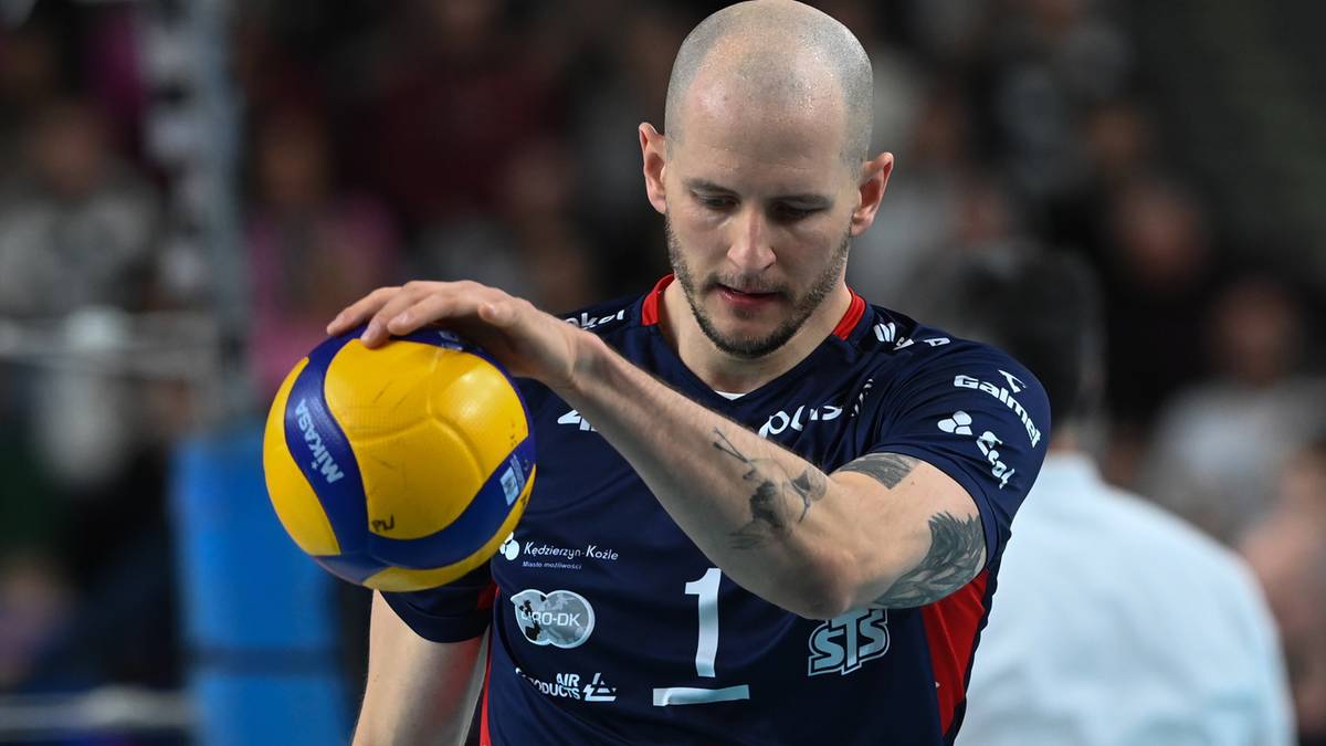 Mężczyzna w niebieskiej koszulce sportowej z numerem 1 i żółto-niebieską piłką do siatkówki w dłoni.