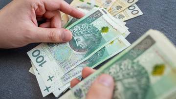 Dłonie trzymające stosy polskich banknotów o nominałach 100 i 200 złotych.