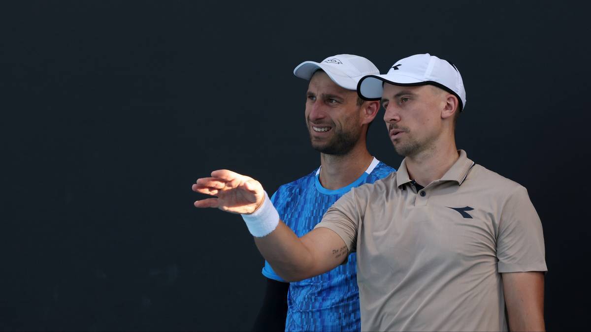 Dw&oacute;ch białych tenisist&oacute;w w czapkach i koszulkach sportowych, patrzących w tym samym kierunku.