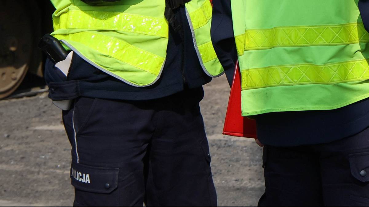 Dwóch mężczyzn w kamizelkach odblaskowych, jeden w czapce policyjnej, stoi obok żółtego tramwaju.