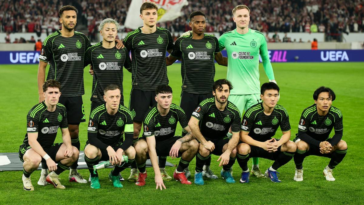 Drużyna piłkarska w zielonych i czarnych strojach pozuje do zdjęcia na murawie stadionu.