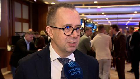 Piotr Pykel w okularach i garniturze rozmawia przed mikrofonem Polsat Sport.