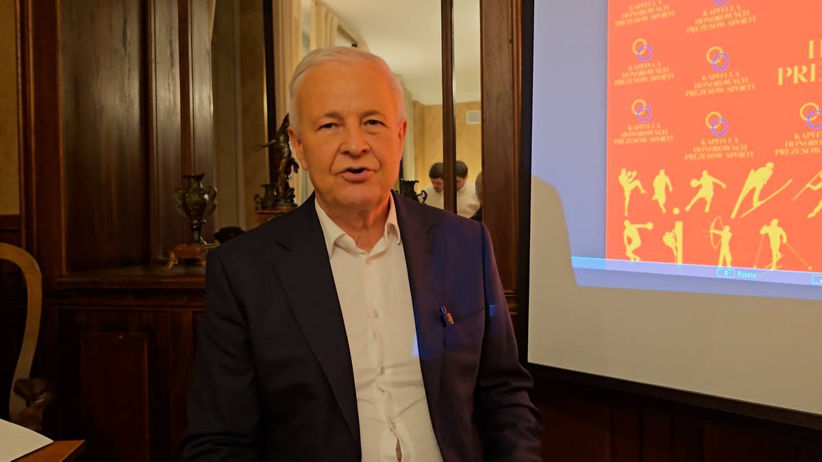 Andrzej Tajner, prezes Polskiego Związku Narciarskiego, w czarnym garniturze i białej koszuli, stoi na tle sali konferencyjnej.
