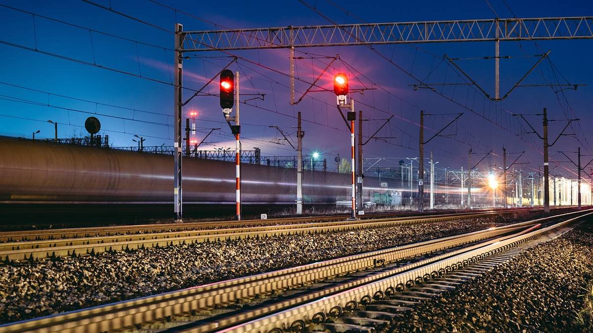 Widok na nocną, oświetloną linię kolejową z semaforami sygnalizującymi czerwone światło.