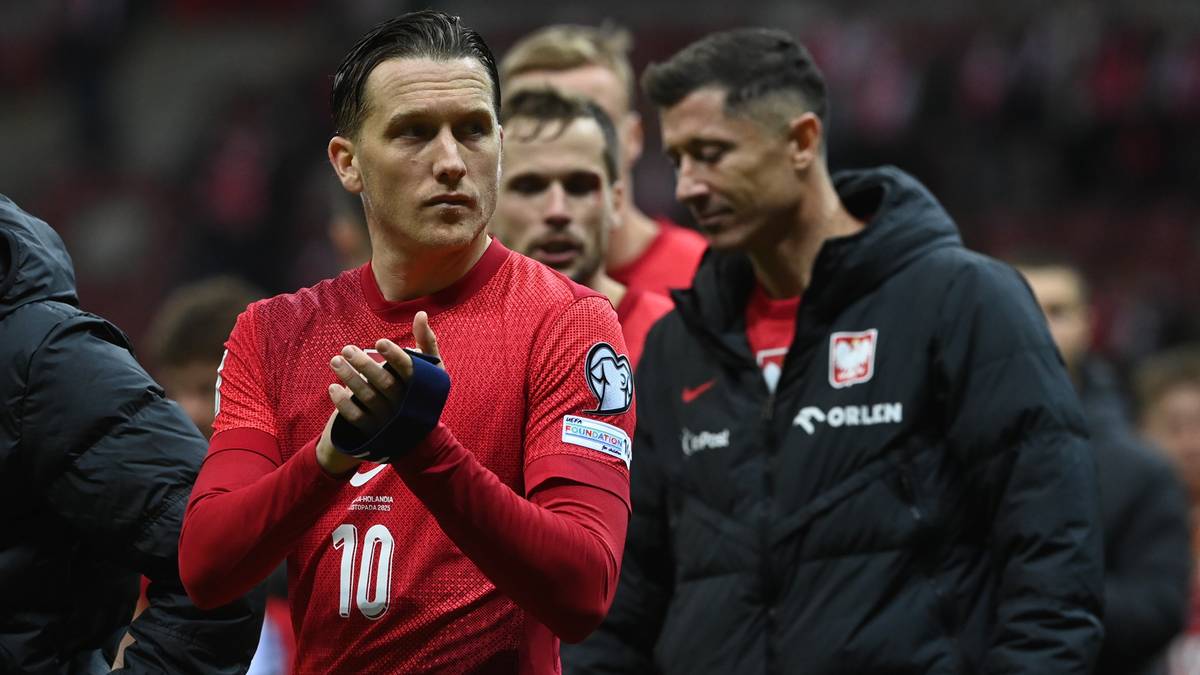 Piłkarz w czerwonej koszulce z numerem 10 i Robert Lewandowski w kurtce reprezentacji Polski na boisku.