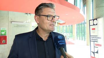 Adam Korol w ciemnej marynarce i okularach udziela wywiadu, trzymając mikrofon z logo Polsat Sport.