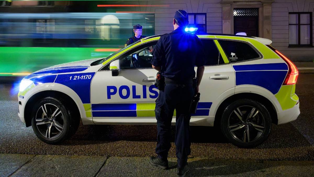 Szwedzki radiow&oacute;z policyjny z włączonymi sygnałami świetlnymi i stojącym obok policjantem.