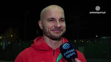 Portret Piotra Michalskiego, ogolonej głowy, z brodą, uśmiechniętego, trzymającego mikrofon z logo Polsat Sport.