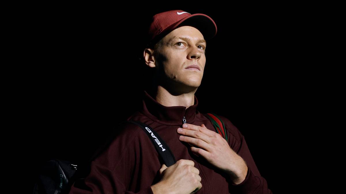 Mężczyzna w sportowym ubraniu i czapce, z torbą na ramieniu, patrzący w bok.